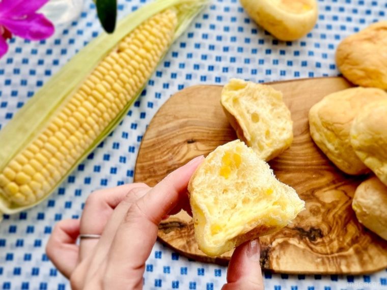 ウッドボードの上でカットしたコストコのコーンブレッドロールを半分手で持っているところ、皮を半分むいたコーン