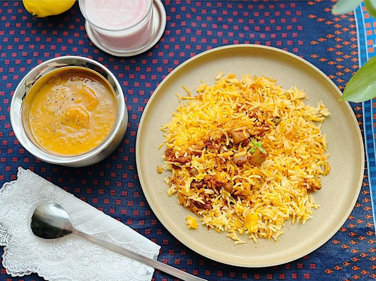 皿に盛ったコストコのベジタブルビリヤニ、ステンレスの器に入ったカレー、グラスに入ったラッシー、白いナプキン