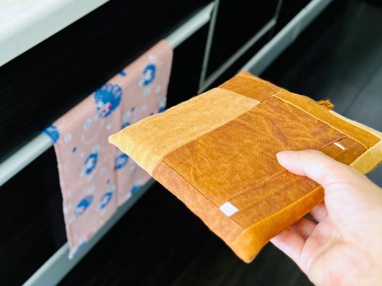 シンク下にかかった手ぬぐいと、手で持った鍋敷き