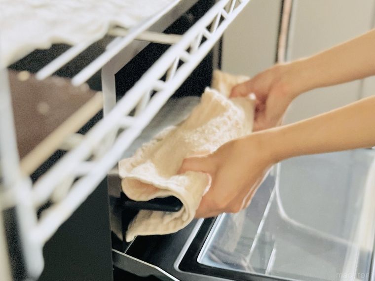 厚手のタオルを鍋つかみ代わりにして天板を持っている様子