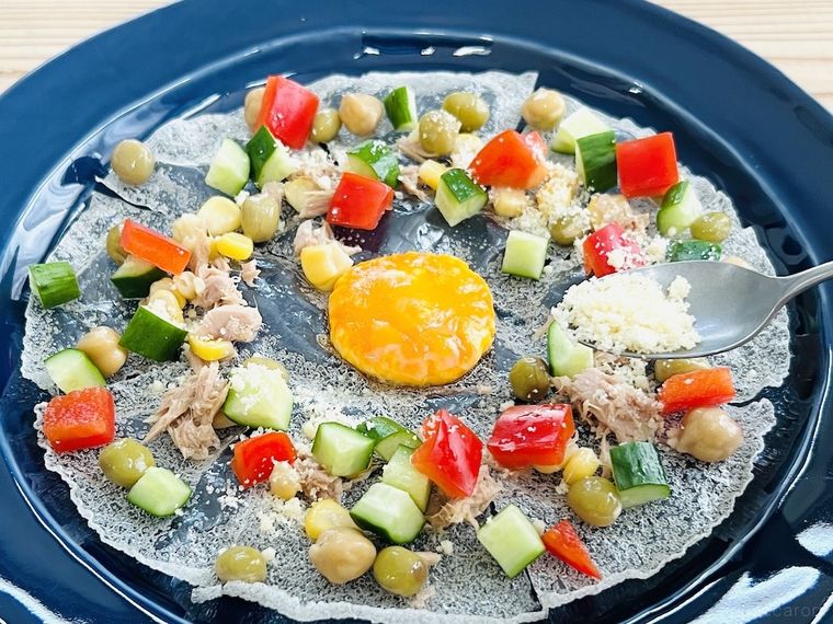 卵黄をのせて揚げたライスペーパーにサラダの具材をトッピングしている様子