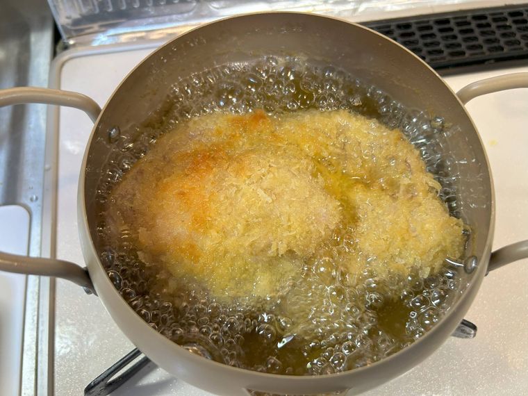 ベージュの鍋で豚ロース肉を揚げる様子