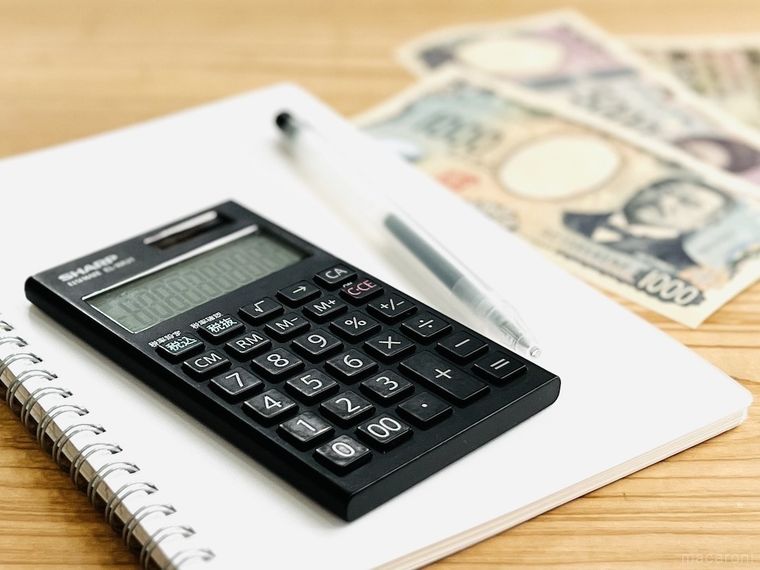 テーブルの上に電卓、ノート、ボールペン、お金が置かれている
