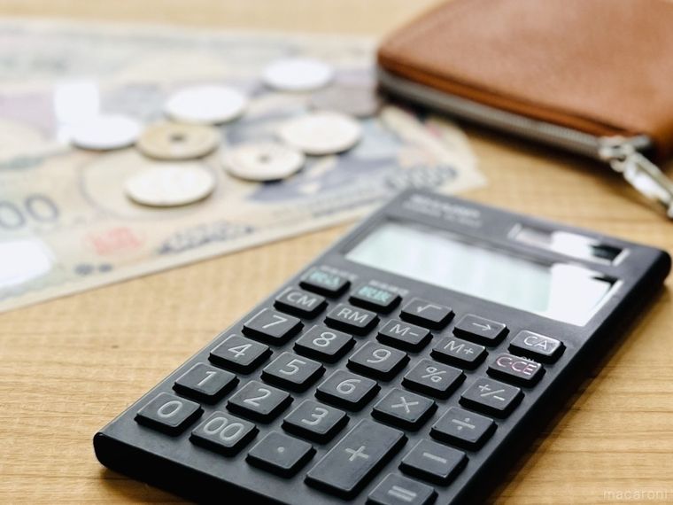 テーブルの上に電卓、お金、財布が置かれている様子