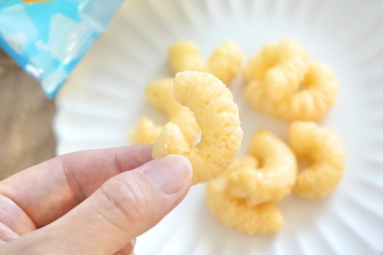 木のカッティングボードと白い皿にのったバニラ風味のキャラメルコーンを手に持つ様子