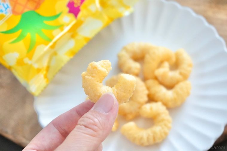 木のカッティングボードと白い皿にのったパイン風味のキャラメルコーンを手に持つ様子