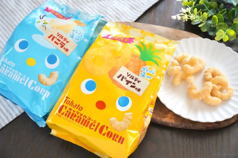 木のカッティングボードと白い皿にのったキャラメルコーンと水色と黄色のパッケージとストライプの布とグリーン