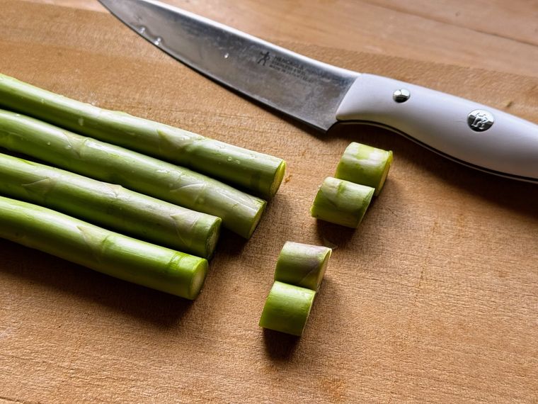 木のカッティングボードにのった根元をカットされた4本のアスパラとナイフと