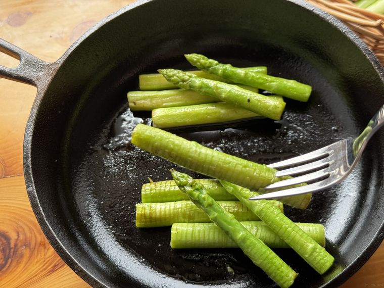 フォークで持ち上げたアスパラソテーと黒い鉄のフライパン