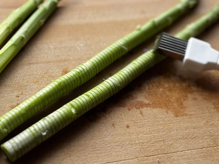 木のカッティングボードにのった2本のアスパラとネギカッター