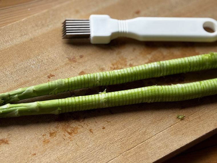 木のカッティングボードの上に置かれた筋切りされたアスパラとネギカッター