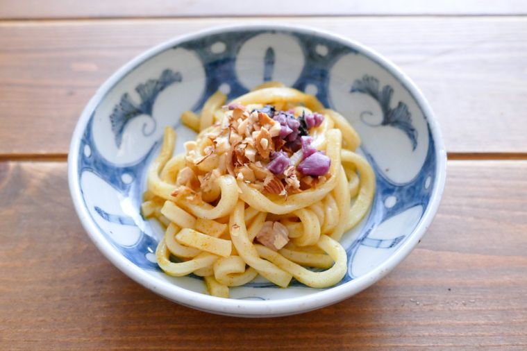 砕いたナッツと刻んだ柴漬けをトッピングした汁なしカレーうどん