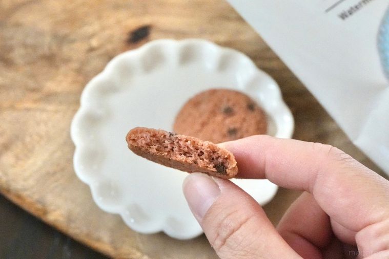 木のカッティングボードと白い皿にのったすいか味のチョコチップクッキーの断面と手に持つ様子
