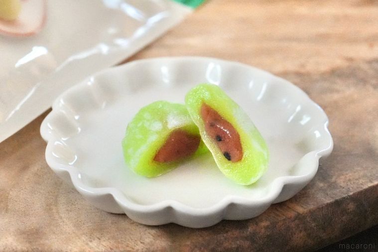 木のカッティングボードと白い皿にのった緑色のすいか味の大福の断面とパッケージとストライプの布とグリーン