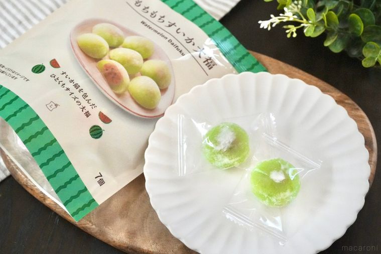 木のカッティングボードと白い皿にのった緑色のすいか味の大福とパッケージとストライプの布とグリーン