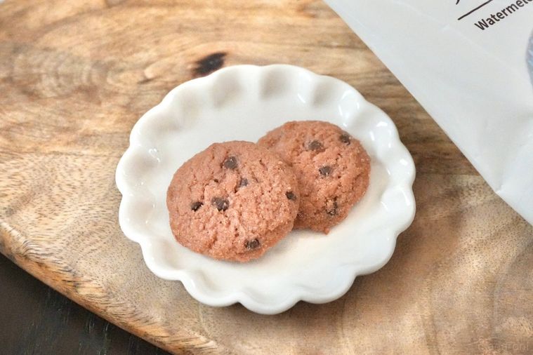 木のカッティングボードと白い皿にのったすいか味のチョコチップクッキーとパッケージの袋