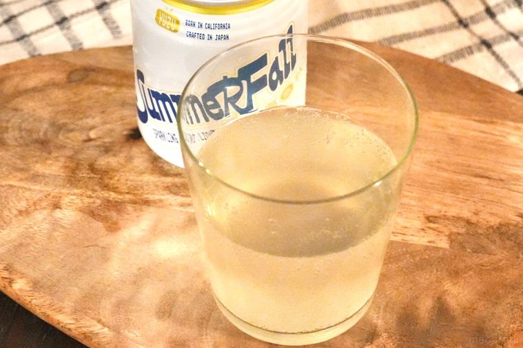 木のカッティングボードにのった日本酒スパークリングの白と黄色のパッケージ缶とグラスと生成色の布