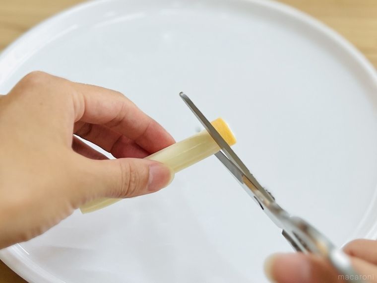 「ポテコ」を通した「さけるチーズ」をキッチンバサミで切っている様子
