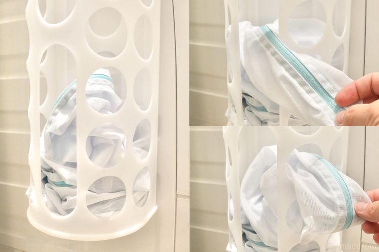 丸い穴が開いた白いプラスチック製の袋ディスペンサーに洗濯ネットを入れて手で引き出す様子