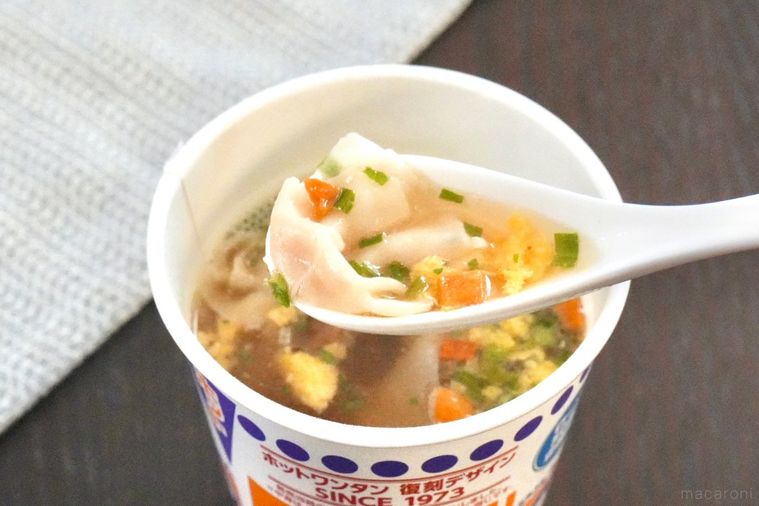 ホットワンタンカップスープを白いレンゲですくって食べる様子とグレーの布
