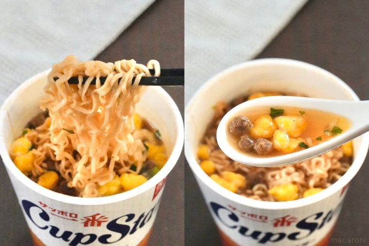 茶色いテーブルとしょうゆ味のカップラーメンの麺を黒い箸で食べ白いレンゲでスープをすくう様子