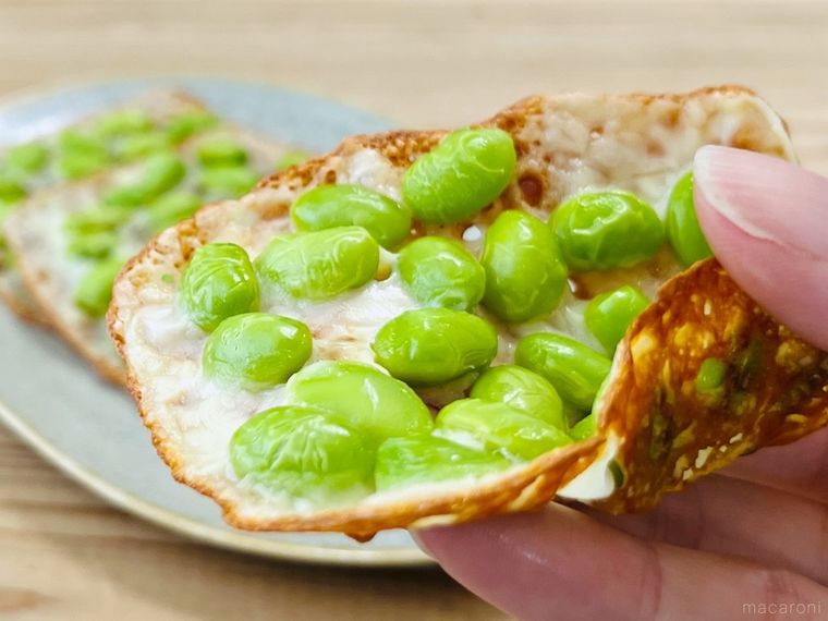 枝豆をのせて焼いたスライスチーズを手で持っている様子