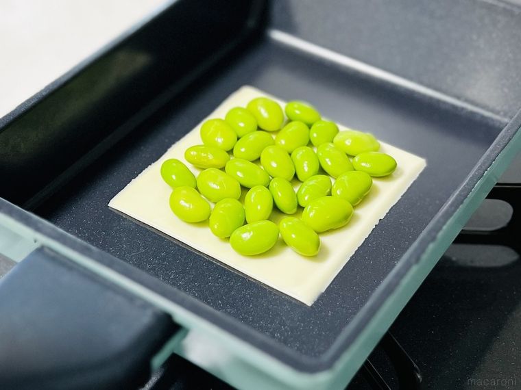 フライパンにとろけるチーズをのせ、その上にむき枝豆をのせた様子