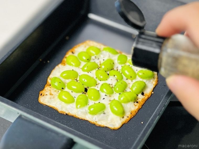 枝豆をのせて焼いたスライスチーズに粗挽き黒こしょうを振っている様子