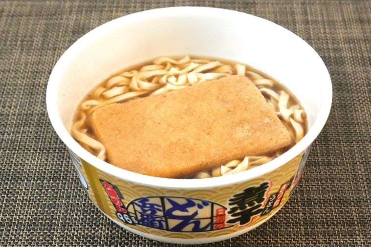 茶色いランチョンマットと大きなお揚げがのった煮干し味のカップうどんのできあがりの様子