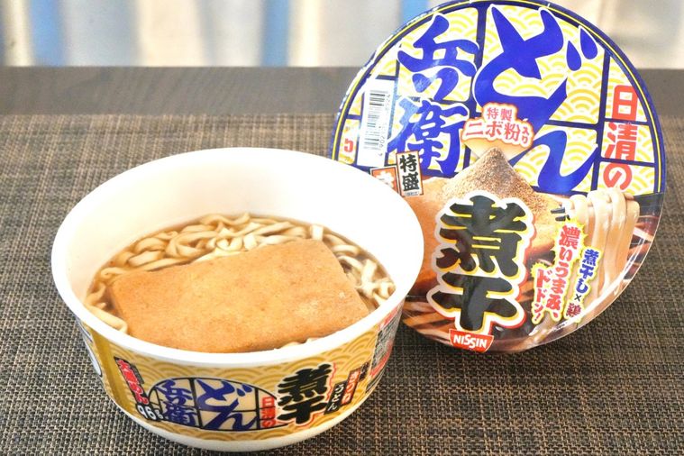 茶色いランチョンマットと煮干し味のカップうどんとフタのパッケージ