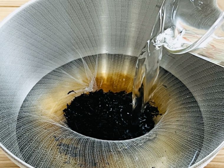 水きりネットをかぶせたボウルにひじきを入れて、水をそそいでいる様子