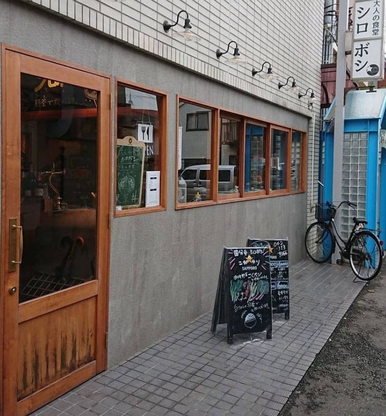 コンクリートの壁に木枠の入り口や窓が並ぶ大人の食堂 シロボシの外観