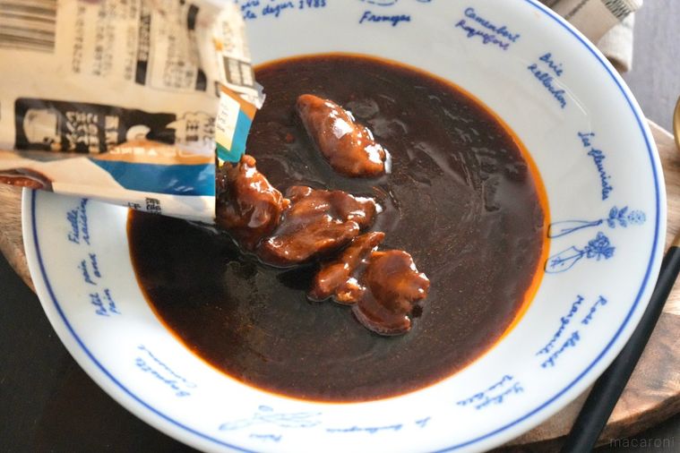 木のカッティングボードにのった白い器に牛タンビーフシチューを袋から出して盛る