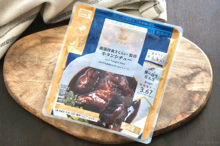 木のカッティングボードにのった牛タンシチューのレトルトパッケージと生成色の布