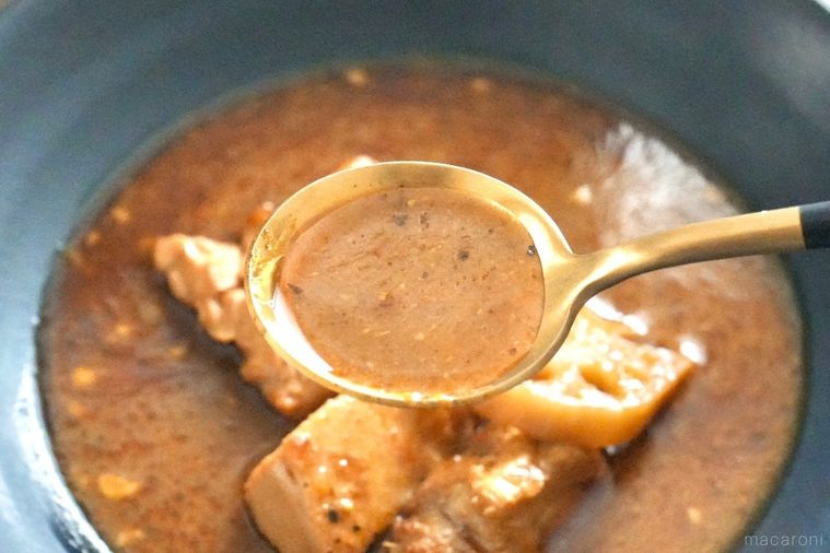 黒い皿に盛られたスープカレーを金と黒色のスプーンですくう様子