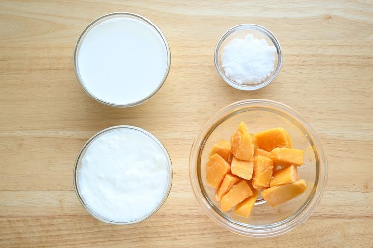 冷凍マンゴーとヨーグルト、牛乳、砂糖がテーブルの上に並んでいる