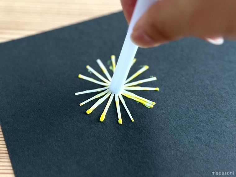 ストローで作ったスタンプに黄色い絵の具をつけて、黒い画用紙に押している様子