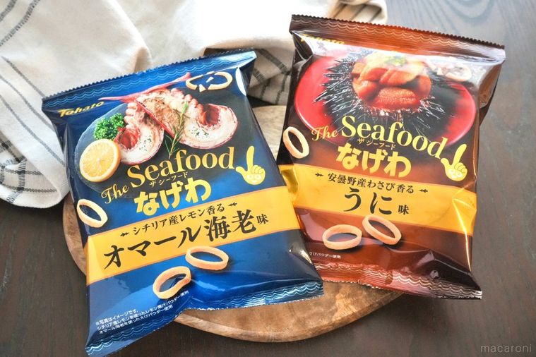 木のカッティングボードにのった青色と赤色のパッケージのポテトリングスナックと生成色の布