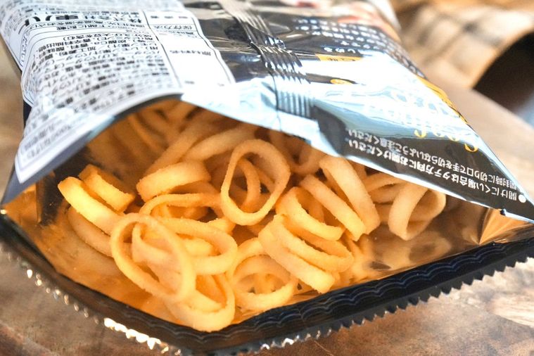木のカッティングボードにのった黒いパッケージの中身のオマール海老味のポテトリングスナック
