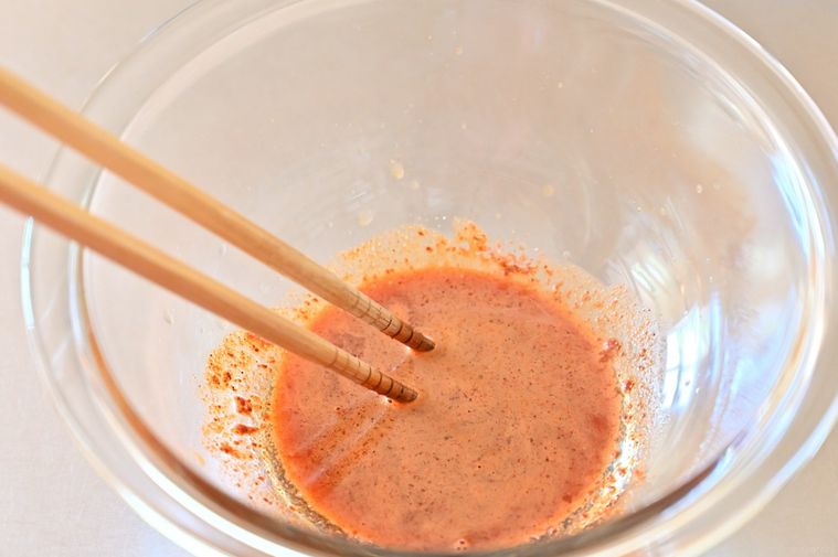 ガラスボウルに入った赤い調味料を箸で混ぜている