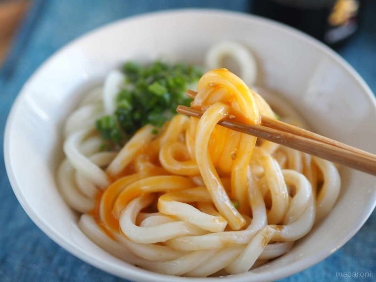 釜玉うどんに卵の黄身を絡めて箸ですくった写真