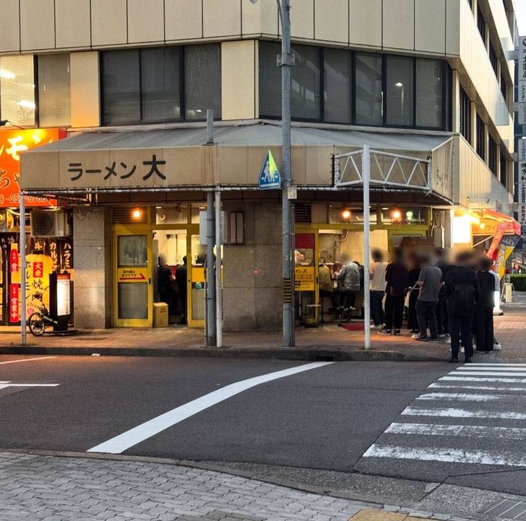 黄色い日よけ看板がかかり行列ができているラーメン大 名古屋店の外観
