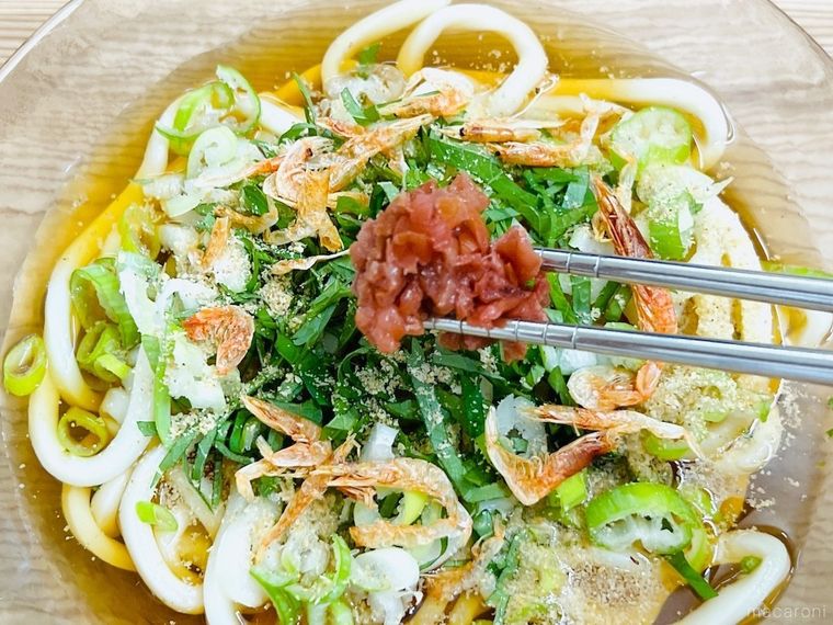 うどんに梅干し、桜えび、すりごま、ねぎ、大葉をトッピングしている様子