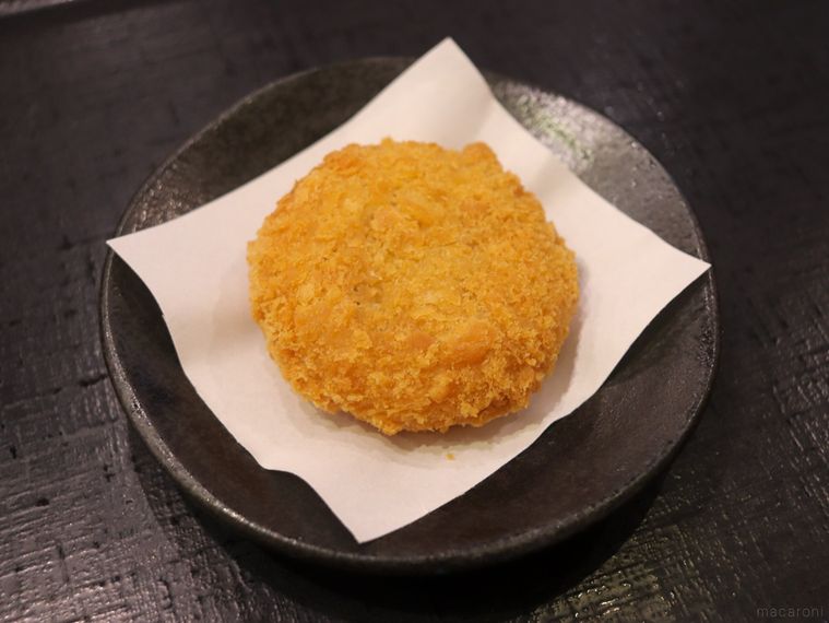 黒い平皿に置かれている山下本気うどんの肉じゃがコロッケ