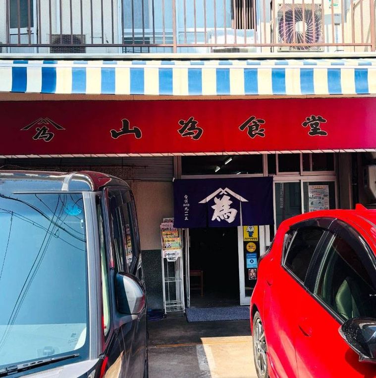 赤い日よけ看板と紺色ののれんがかかった山為食堂の外観