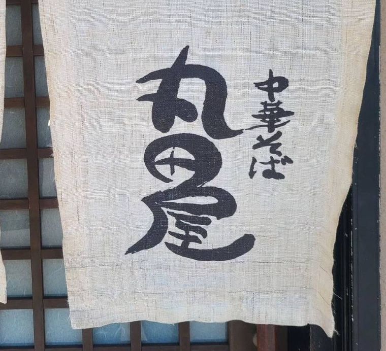 白い店名入りののれんがかかった中華そば 丸田屋 岩出本店の入り口