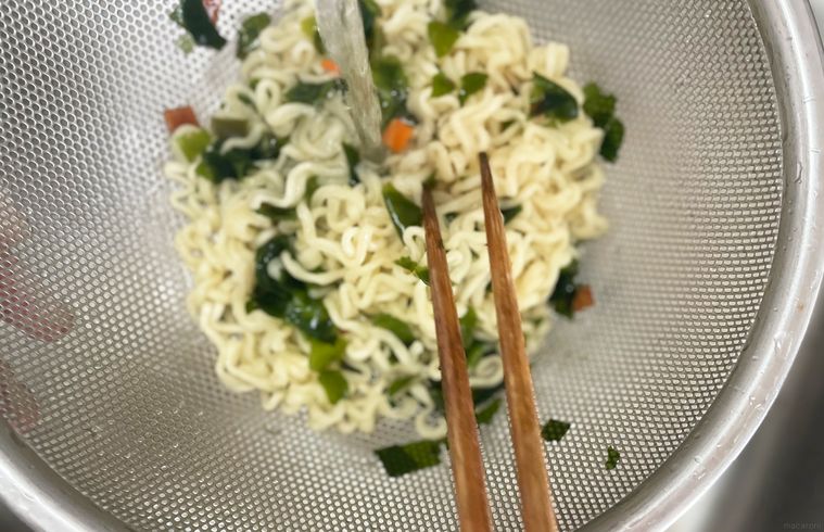 ゆでたラーメンをザルにあげて水で冷やしている写真