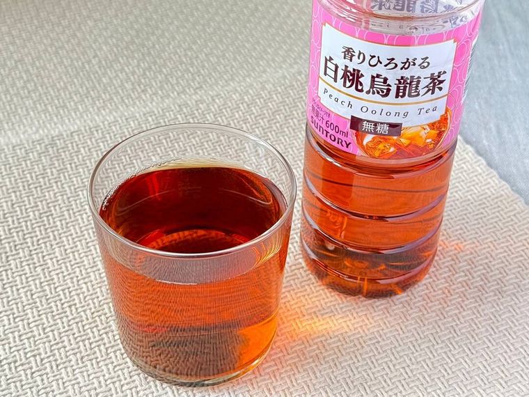 グラスに注いだサントリー白桃烏龍茶とパッケージが並んでいる様子