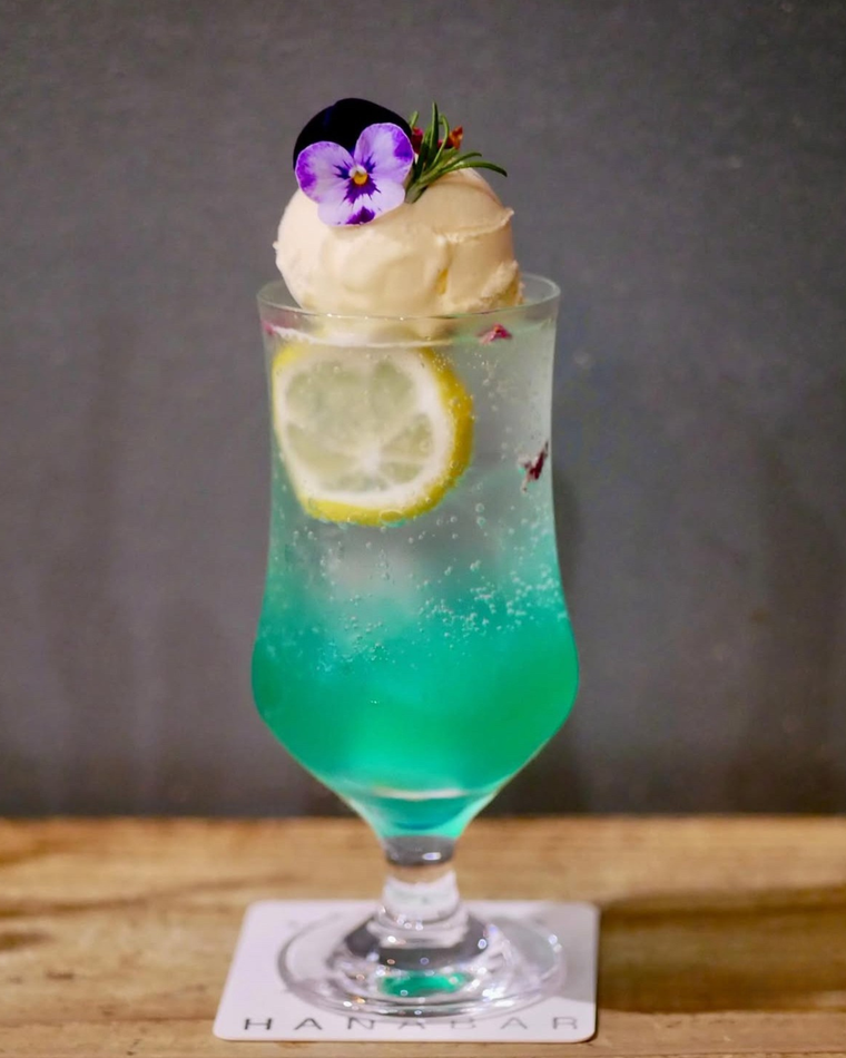 青緑色のソーダにレモンスライスとバニラアイスを浮かべ、エディブルフラワーで飾った華やかなクリームソーダ