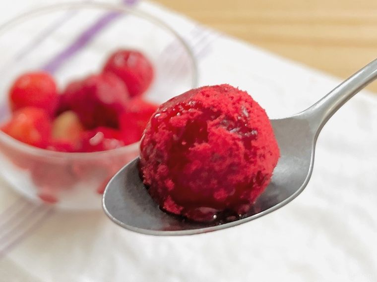 ラズベリーパウダーをまぶしたアイスの実をスプーンですくった様子